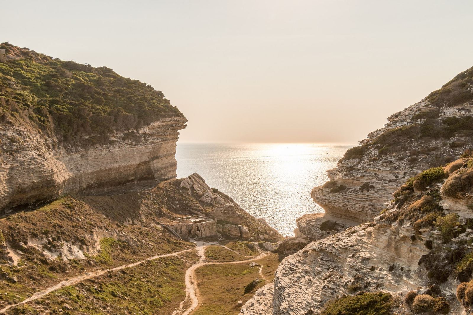 Une piste de terre serpente entre deux falaises corses face à la mer, au couchant